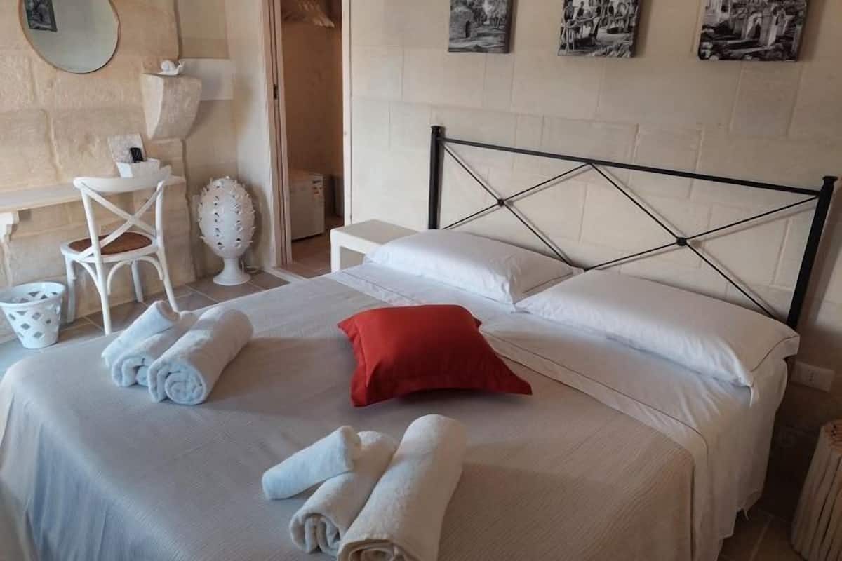 A neatly made bed with white linens, a red pillow, and rolled towels.