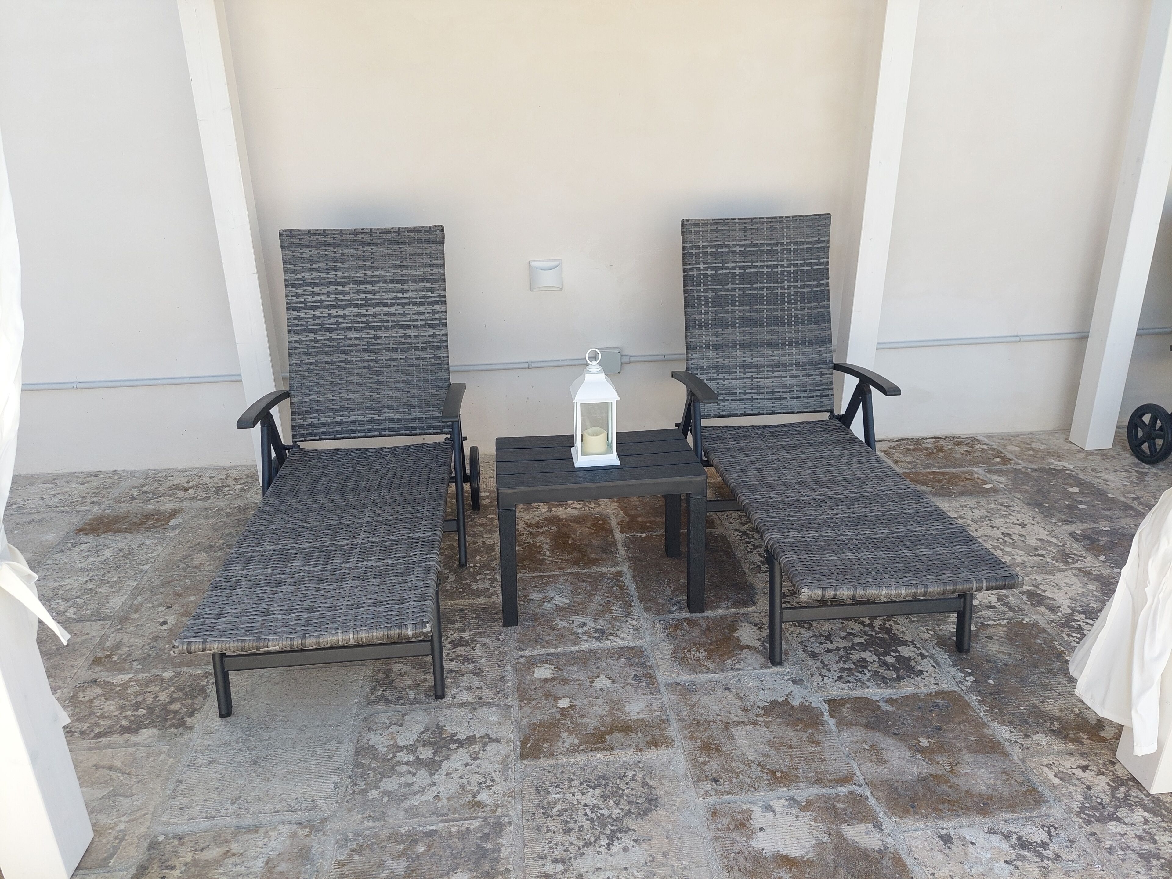 Duas cadeiras de vime com uma mesinha e um candeeiro entre elas, num terraço de pedra.
