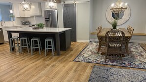 Une cuisine moderne dotée d’un îlot central, de tabourets de bar et d’un coin repas avec une table et des chaises en bois.