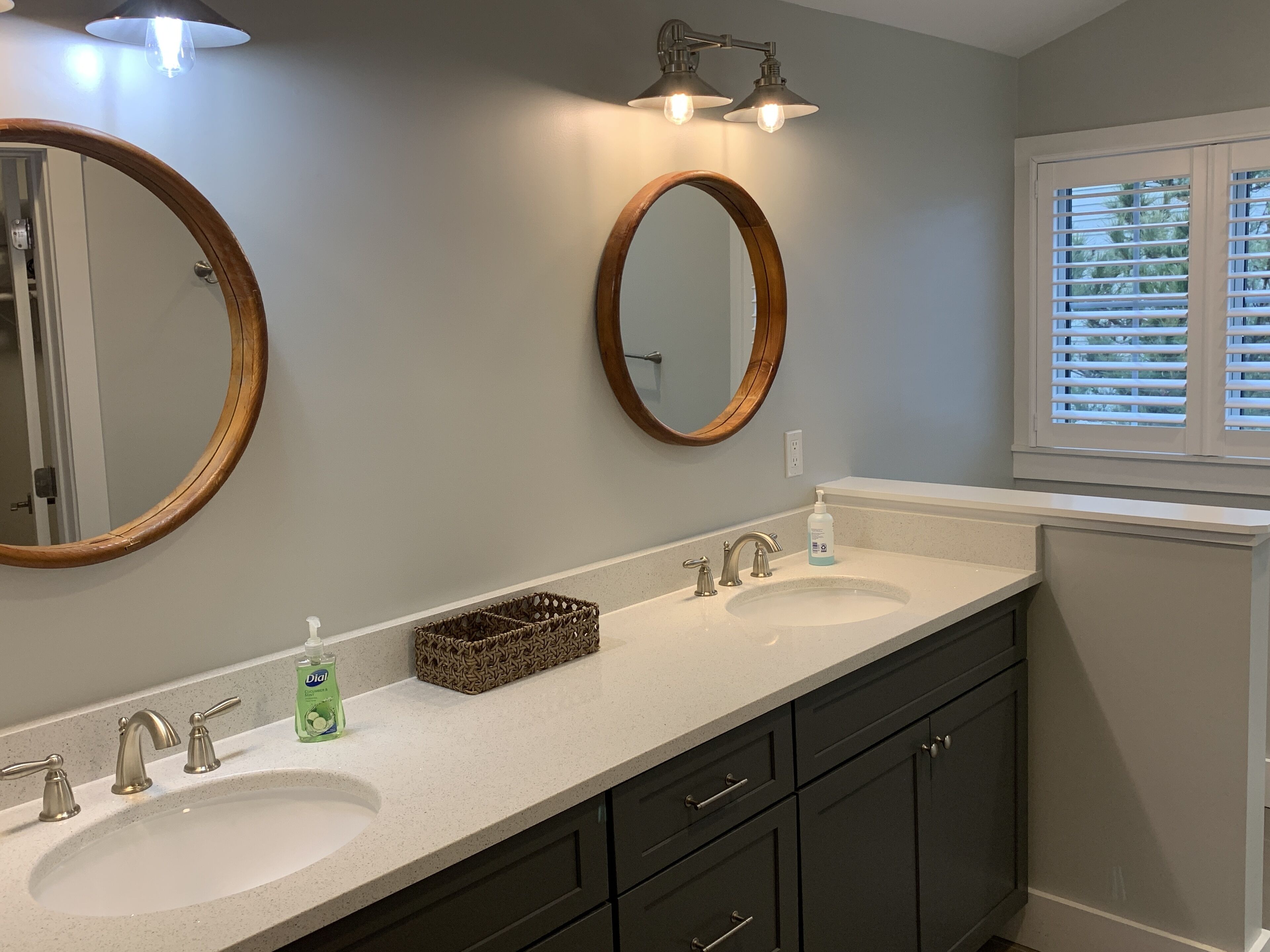 Une salle de bain avec deux lavabos, des meubles sombres et une fenêtre avec des stores.