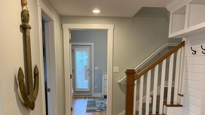 Un couloir au plancher en bois, un escalier avec des rampes blanches et une ancre décorative accrochée au mur.
