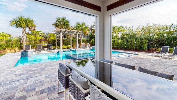 A modern outdoor pool area with a glass table and chairs, surrounded by lush greenery and a pergola. - Chic Mansion with Games Room (Kissimmee)