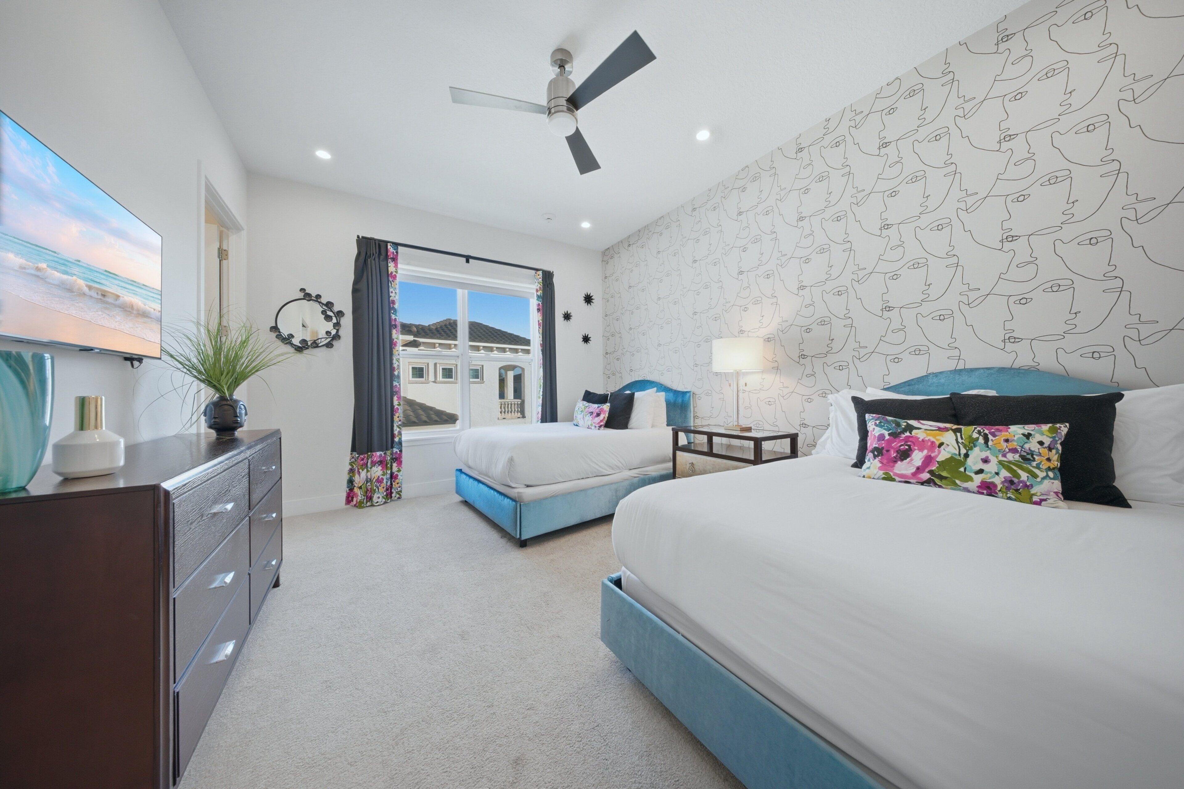 Quarto com cama, penteadeira, ventoinha no teto, televisão e janela com cortinas.