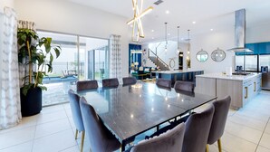 A modern kitchen with a central island, a dining area with a glass table, and a staircase leading to an upper level. - Chic Mansion with Games Room (Kissimmee)