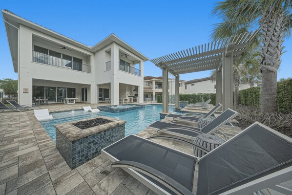 A pool area with lounge chairs, a pergola, and a two-story building with balconies. - 8BR Estate | Reunion Water Park & Resort Pools (Kissimmee)