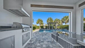 An outdoor kitchen with a grill, a pool with lounge chairs, and a pergola. - Chic Mansion with Games Room (Kissimmee)