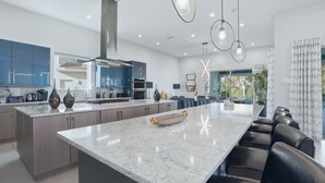 A modern kitchen with a large island, built-in appliances, and pendant lighting. - Chic Mansion with Games Room (Kissimmee)