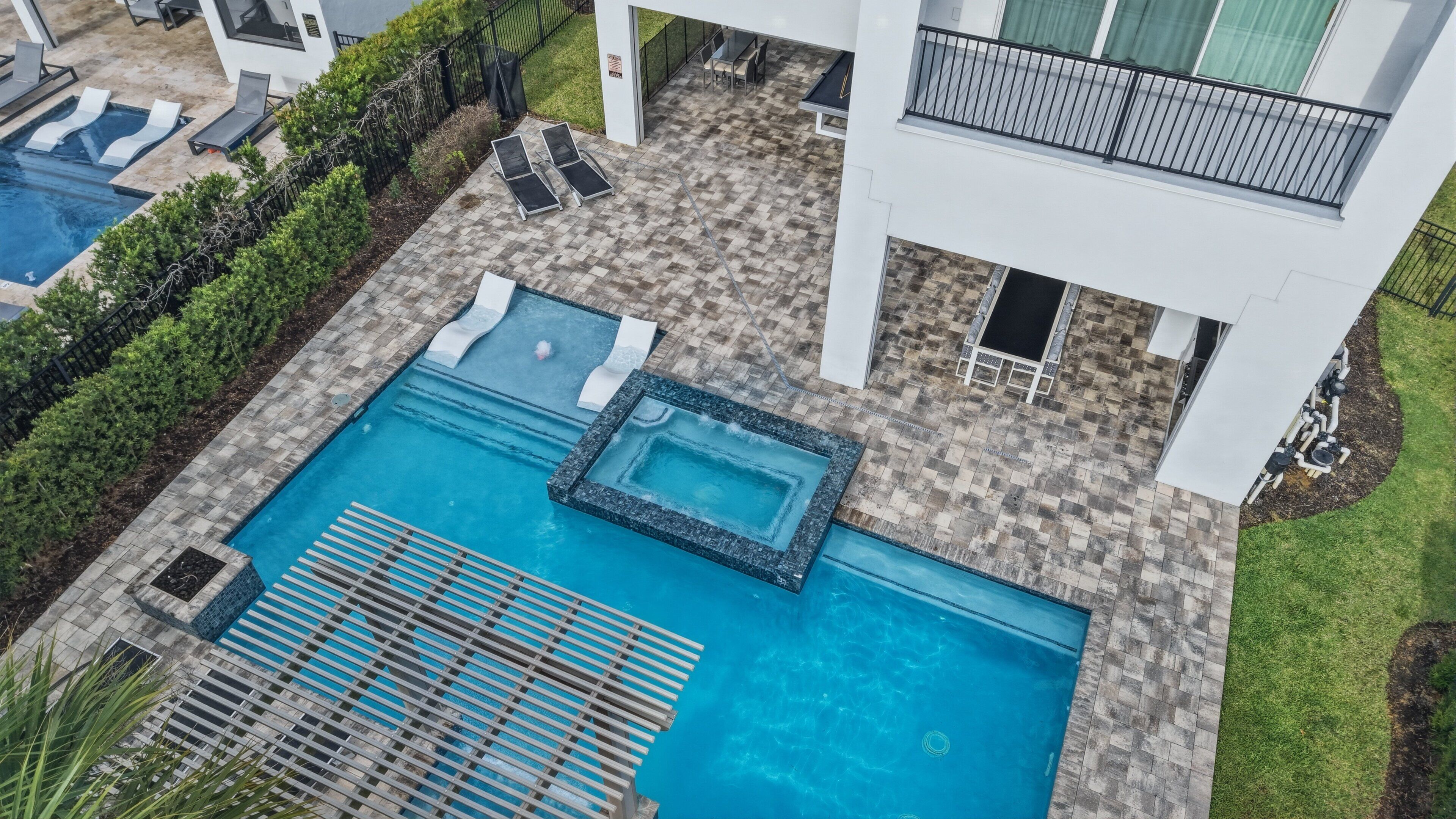 A rooftop pool area with two pools, lounge chairs, and a hot tub.