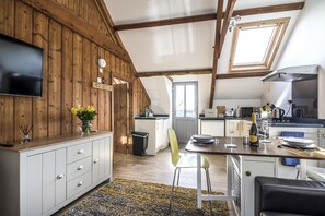 A cozy kitchen with wooden beams, a dining area with a table and chairs, and a TV mounted on the wall. - Ashgrove Farm - 1 Bedroom Apartment - Llawhaden (Narberth)
