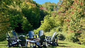 Terraza con sillones Adirondack y una chimenea, con vista a un lago.