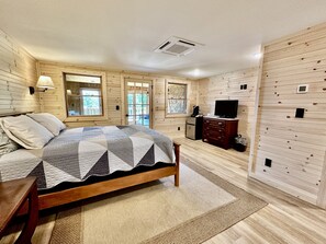 A bedroom with a wooden bed, a dresser, a television, and a window with a view of the outdoors.