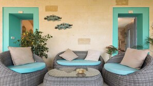A seating area with wicker furniture and teal cushions, a glass coffee table, and decorative wall art. - Tenuta Donna Caterina by BarbarHouse (Mesagne)