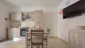 Une cuisine moderne avec un coin repas, dotée de meubles en bois clair, d’un four encastré et d’un téléviseur à écran plat fixé au mur.