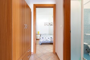 A narrow hallway leading to a bedroom with a bed and a nightstand.