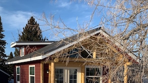 A log cabin with a wooden deck, large windows, and a snow-covered ground. - Downtown Cozy Red Cabin (Victor)