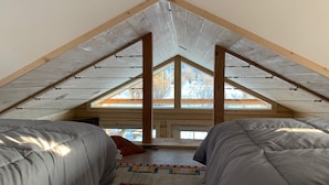 A loft bedroom with a sloped ceiling, wooden beams, and a large window. - Downtown Cozy Red Cabin (Victor)