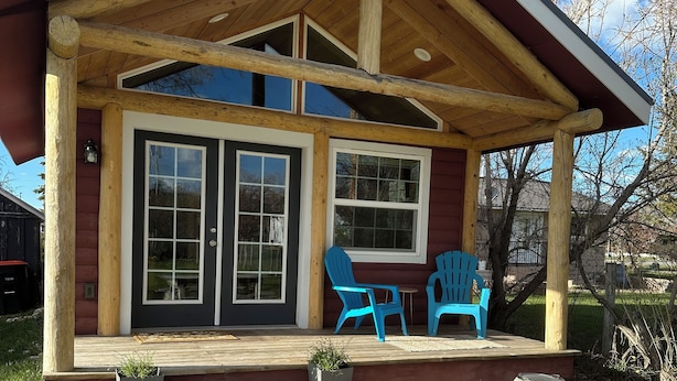A wooden cabin with a porch, two blue chairs, and a stone pathway leading to the entrance. - Downtown Cozy Red Cabin (Victor)