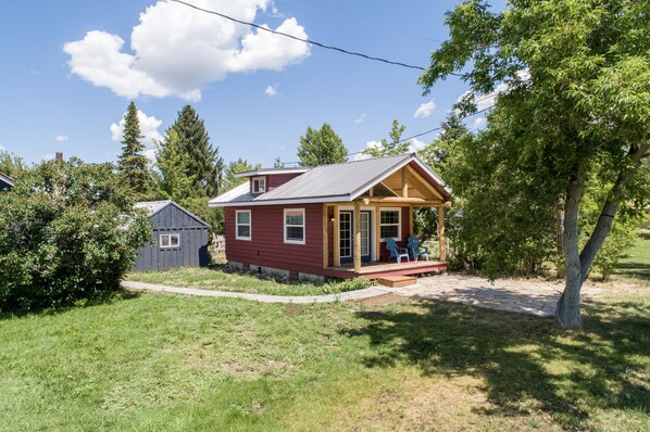 A small, single-story house with a porch and a small shed in the background. - Downtown Cozy Red Cabin (Victor)