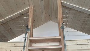 A wooden ladder leading to a lofted sleeping area with a sloped ceiling. - Downtown Cozy Red Cabin (Victor)