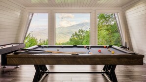 Ein Billardtisch mit Blick auf eine malerische Berglandschaft durch große Fenster.