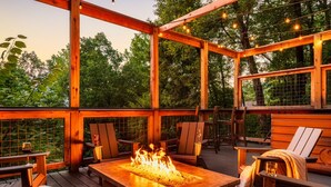 Eine Terrassenanlage im Freien mit Feuerstelle, Holzmöbeln und Lichterketten.