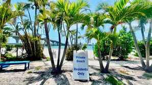 A sign indicating a private beach area for residents only, with palm trees and a bridge in the background. - Lovers Key Beach Club 1105 - Private Beach (Bonita Springs)