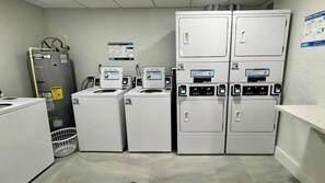 A laundry room with stacked washers and dryers, a water heater, and a wall-mounted instruction poster.