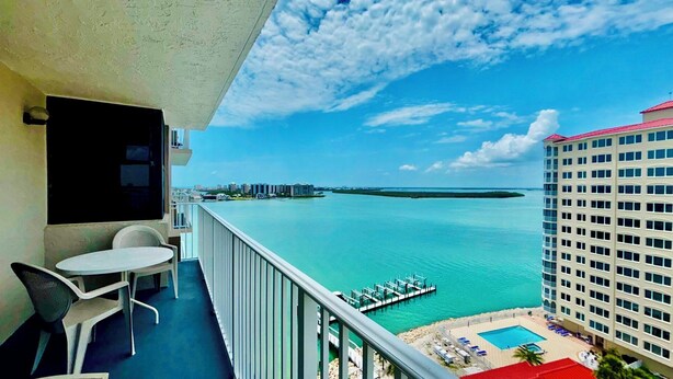 A balcony with a view of a marina, a pool area, and a distant cityscape. - Lovers Key Beach Club 1105 - Private Beach (Bonita Springs)