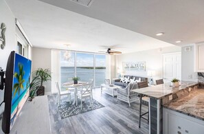 A modern kitchen with a marble countertop, white cabinetry, and a large window overlooking the ocean.
