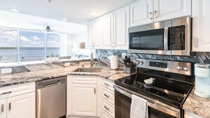 A modern kitchen with white cabinets, a stainless steel microwave, a black stove, and a marble countertop.