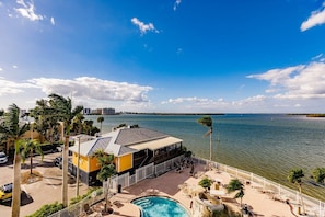 A waterfront property with a pool, outdoor seating, and a building with a sloped roof.