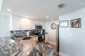 A kitchen with white cabinets, a granite countertop, a stainless steel refrigerator, and a microwave. - Southern Comfort - Updated Waterfront Condo (Bonita Springs)