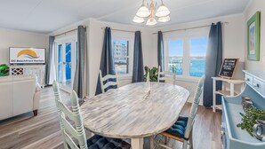 A dining area with a round table, chairs, a chandelier, and a view of the sea through large windows.