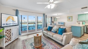 A living room with a sofa, a TV, a coffee table, and a view of the ocean.