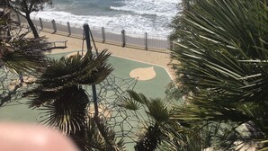A coastal view with a beach, a fence, and palm trees. - Cosy studio for 2 near the beach (Sanary-sur-Mer)