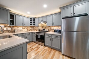 Una cocina moderna con gabinetes grises, un refrigerador de acero inoxidable, horno empotrado y salpicadero con diseño de mosaicos.