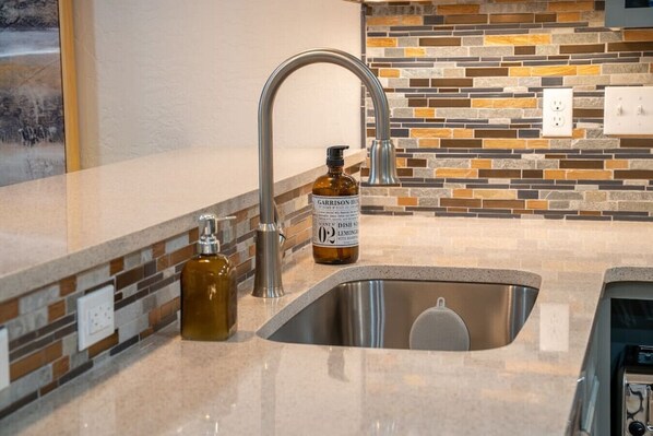Una cocina moderna con un lavamanos de acero inoxidable, un dispensador de jabón y una botella de detergente.