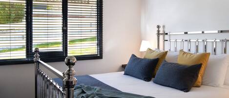 Une chambre d’hôtel avec un lit, des oreillers, un radiateur et une fenêtre avec des stores.