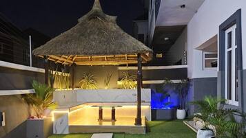 A modern outdoor space with a thatched gazebo, a marble counter, and potted plants.