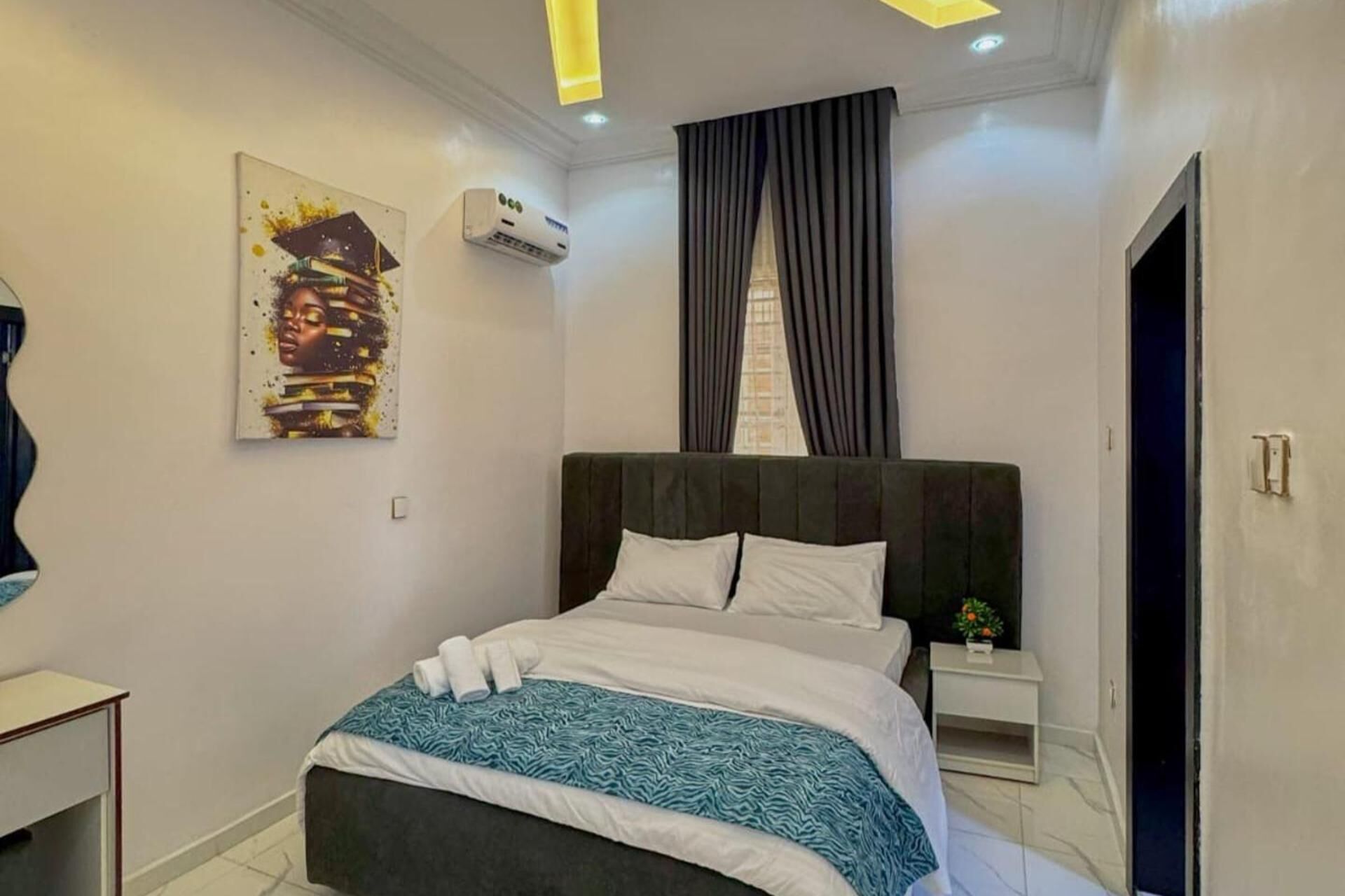 Een moderne slaapkamer met een groot bed, een nachtkastje met een plant erop, en een schilderij aan de muur.