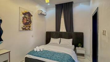 Een moderne slaapkamer met een groot bed, een nachtkastje met een plant erop, en een schilderij aan de muur.
