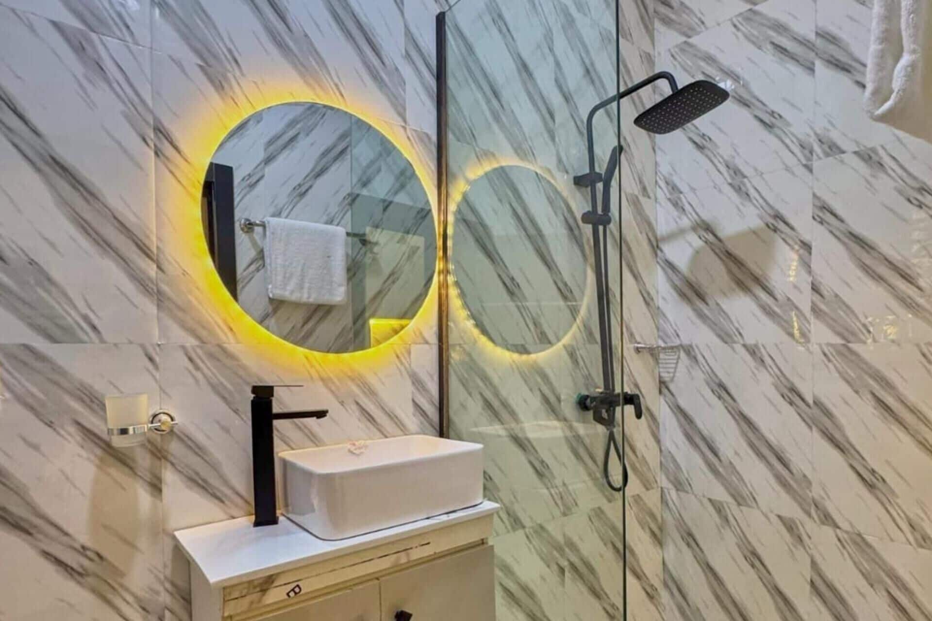 Een badkamer met een marmeren wand, een wastafel met een zwarte kraan en een douche met een handdouche.