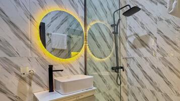 Een badkamer met een marmeren wand, een wastafel met een zwarte kraan en een douche met een handdouche.