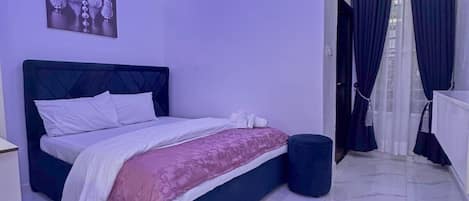 A modern bedroom with a bed, a nightstand, a wall-mounted artwork, and a bathroom with a curtain.
