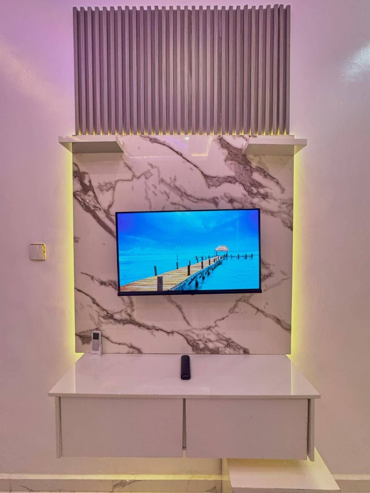Un'elegante mobile TV moderno con televisore piatto, rivestimento murale effetto marmo e illuminazione integrata.