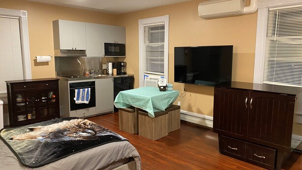 A compact bedroom with a bed, a small table, a TV, a kitchenette, and a wardrobe. - Apt 3C Lake Bomoseen Inn “The Dog” with boat slip.  (Castleton)