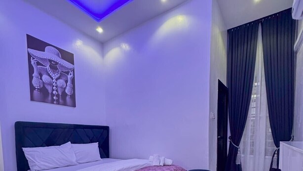 A modern bedroom with a bed, a nightstand, a wall-mounted artwork, and a bathroom with a curtain. - 1 Bedroom Ensuite in a Shared House (Lekki)