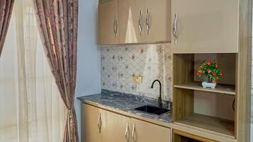 Cocina pequeña y funcional con lavamanos, armarios y un refrigerador compacto.