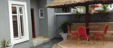 A patio area with a thatched umbrella, red chairs, and a small table.