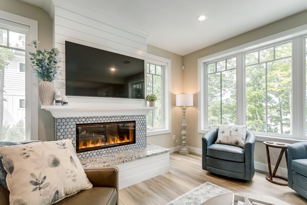 A modern living room with a fireplace, comfortable seating, and large windows.